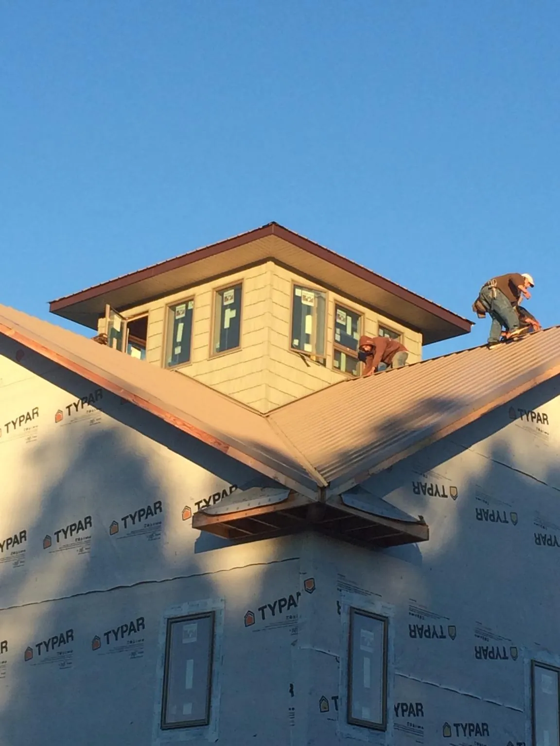 Roofers working around a rooftop cupola on a new metal roof at sunset in Hillsboro